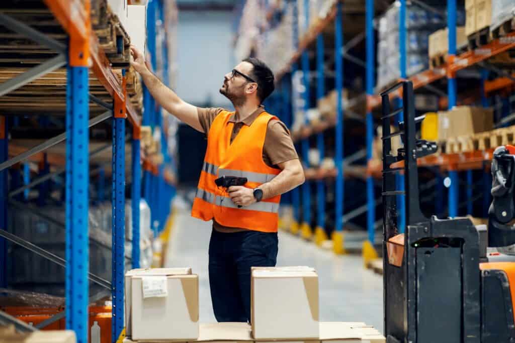 Warehouse operative managing stock beneath a mezzanine floor installation with high-bay racking and safety gear