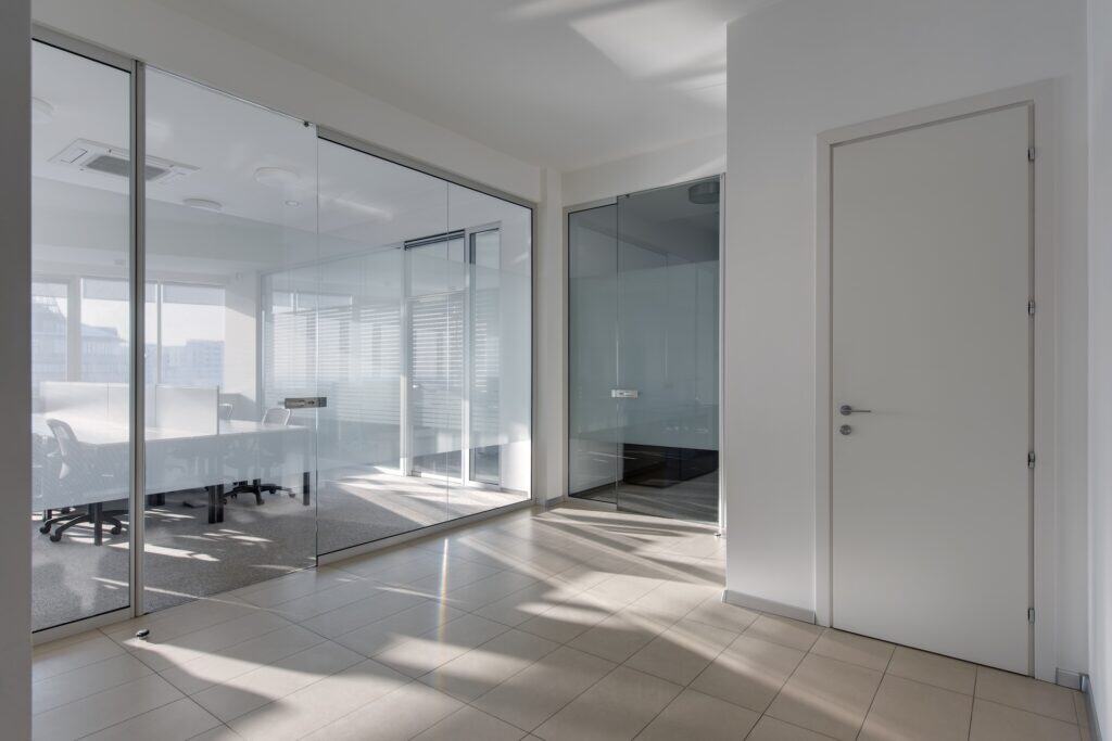 Modern small office with glass partition walls creating separate meeting rooms while maintaining visual openness and natural light flow for space efficiency
